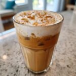 Close-up of a refreshing Brown Sugar Iced Pumpkin Cream Latte with icy layers and thick foam topping dusted with spice.