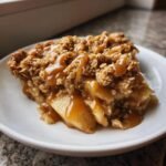 A close-up of a warm slice of Caramel Apple Pear Crisp topped with a generous caramel sauce drizzle.