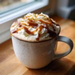 A cozy mug filled with Caramel Pumpkin Spice White Hot Chocolate, topped high with whipped cream and a caramel drizzle.