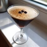 A perfectly frothed Chocolate Espresso Martini in a chilled glass, garnished with three coffee beans.
