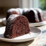 A close-up slice of rich, dark Chocolate Mocha Bundt Cake dusted with powdered sugar on a white plate.