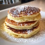 A stack of three thick, fluffy Christmas Morning Eggnog Pancakes dusted heavily with powdered sugar.