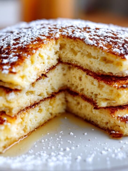 Close-up of a thick stack of fluffy Christmas Morning Eggnog Pancakes dusted with powdered sugar.