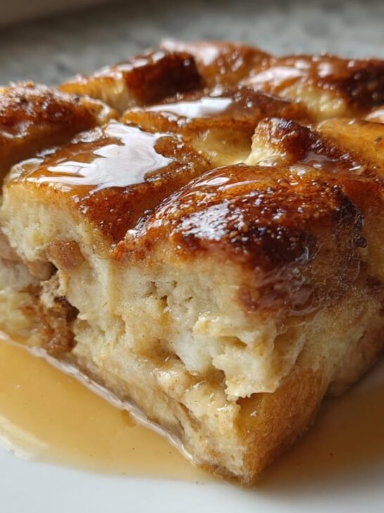 A close-up of a square slice of Cinnamon Brown Butter French Toast Casserole, drizzled with syrup.