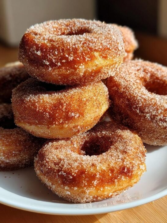A stack of freshly made Cinnamon Sugar Baked Donuts generously coated in sparkling cinnamon sugar, resting on a white plate.