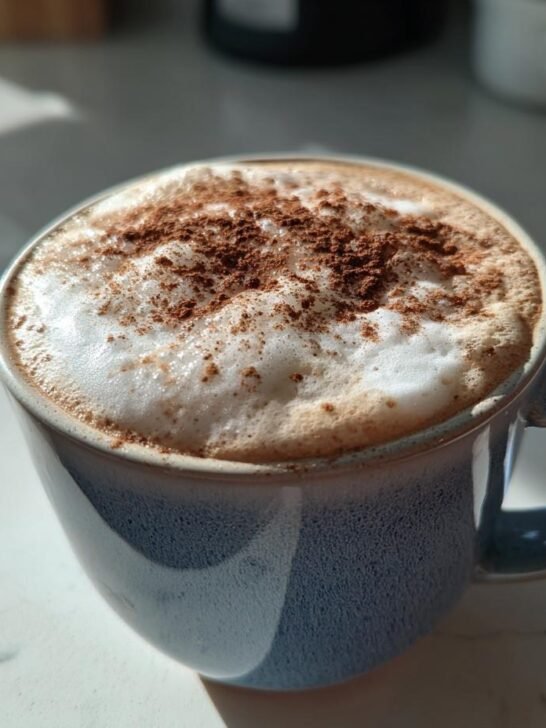 A close-up photo of a Cinnamon Toast Latte in a blue speckled mug, topped with thick foam and cinnamon powder.
