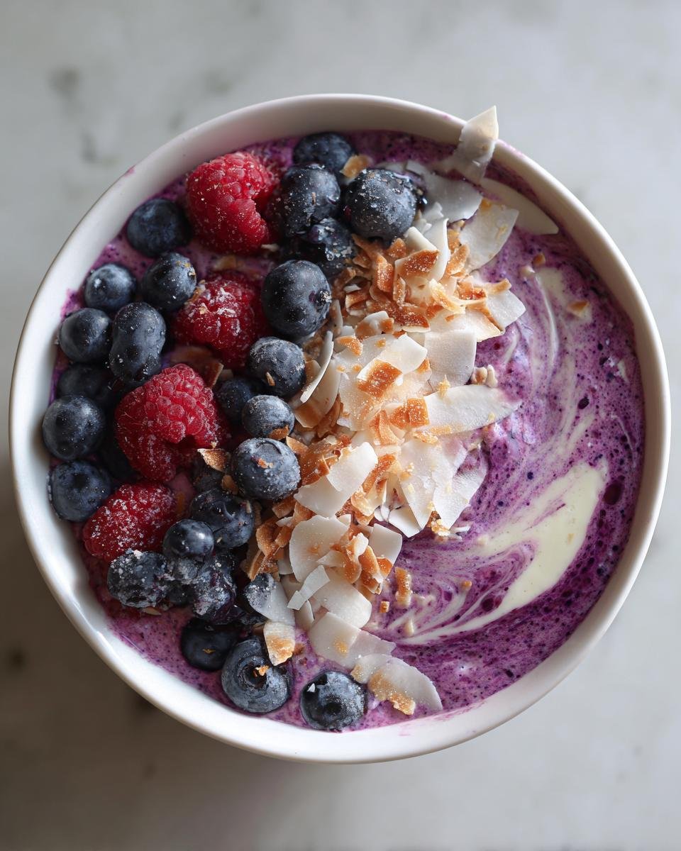 Overhead view of a vibrant Coconut Berry Smoothie Bowl topped with fresh blueberries, raspberries, and toasted coconut flakes.