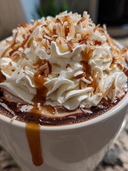 Close-up of Coconut Caramel Hot Chocolate topped with whipped cream, toasted coconut, and caramel drizzle.
