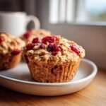 A close-up of a freshly baked Cranberry Apple Oat Muffin topped with dried cranberries and oats.