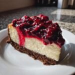 A perfect slice of rich cheesecake with a dark gingersnap crust, topped with vibrant cranberry sauce.