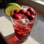 Close-up of a fizzy Cranberry Maple Bourbon Mocktail garnished with fresh cranberries and a lime slice.