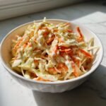 A close-up of creamy coleslaw featuring shredded cabbage and carrots coated in Easy Homemade Coleslaw Dressing in a white bowl.