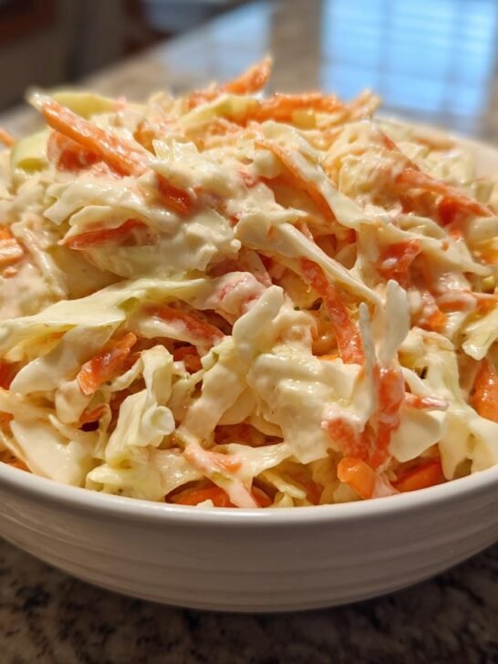 A white bowl filled with creamy coleslaw, featuring shredded cabbage and carrots coated in Easy Homemade Coleslaw Dressing.