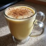 A clear glass mug filled with creamy homemade vegan eggnog, topped with a dusting of cinnamon.