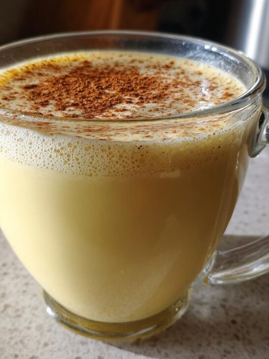 Close-up of a glass mug filled with creamy homemade vegan eggnog, topped with foam and sprinkled cinnamon.