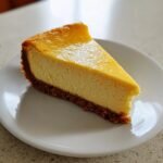 A perfect slice of Creamy Spiced Orange Cheesecake with a thick graham cracker crust, served on a white plate.