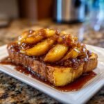 Close-up of thick French toast topped generously with caramelized apples and rich syrup.