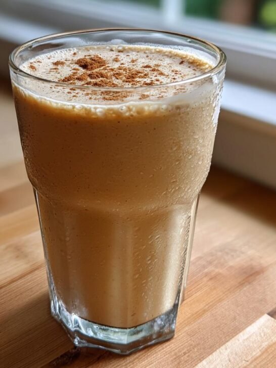 A tall, chilled glass filled with Delicious Vegan Peanut Punch, topped with a sprinkle of cinnamon.