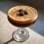 Close-up of a frothy Dirty Chai Espresso Martini Mocktail garnished with three coffee beans.