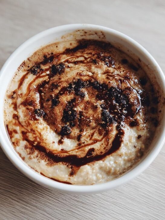 Overhead view of a bowl of creamy Dirty Chai Latte Oatmeal Porridge topped with dark swirls of espresso and spices.