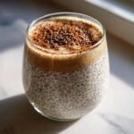 A glass of Easy Make Ahead Chai Latte Chia Pudding topped with cinnamon and whole chia seeds.