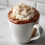 Close-up of rich Eggnog Hot Chocolate topped with a generous swirl of whipped cream and cinnamon.