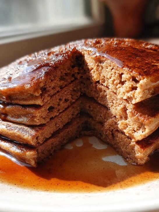 A stack of fluffy Vegan Gingerbread Pancakes cut open to show the texture, drizzled generously with syrup.