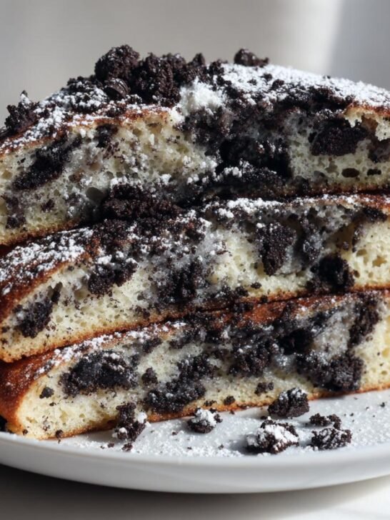 A stack of three fluffy One Bowl Fluffy Vegan Oreo Pancakes cut in half, showing the dark cookie pieces inside and dusted with powdered sugar.
