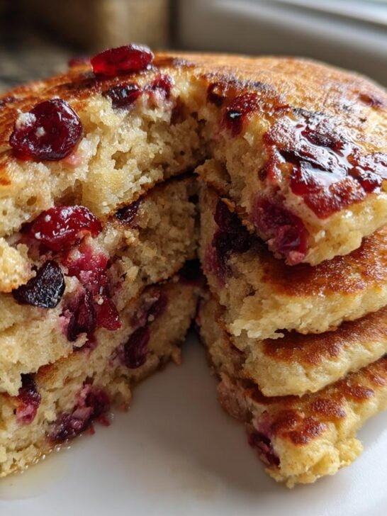 Close-up of a stack of fluffy vegan quinoa pancakes cranberry, cut open to show the texture and fruit inside, drizzled with syrup.