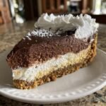 A decadent slice of Gingerbread Truffle Cheesecake showing layers of crust, cream, and chocolate mousse, topped with whipped cream.