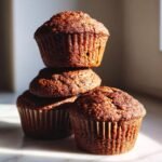 A stack of three richly colored Healthy Vegan Gingerbread Quinoa Muffins catching warm sunlight.