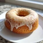 A close-up of a single Homemade Baked Eggnog Donut with thick, dripping eggnog glaze on a white plate.