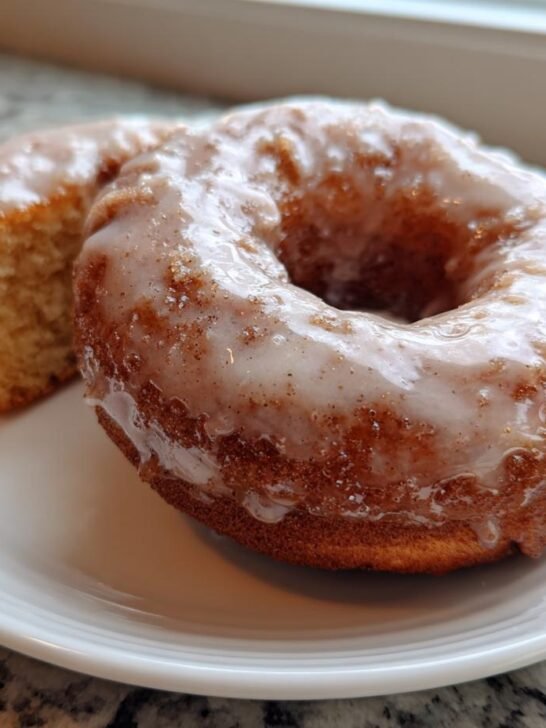 Close-up of a glazed Homemade Baked Eggnog Donut with a slice showing the cake texture next to it.