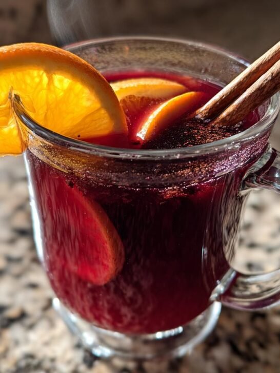 Close-up of steaming Hot Spiced Cranberry Apple Punch garnished with orange slices and cinnamon sticks.