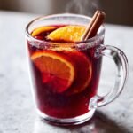 Close-up of steaming Hot Spiced Cranberry Apple Punch garnished with orange slices and a cinnamon stick.