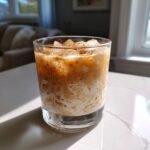 A glass filled with an Iced Maple Cinnamon Oat Latte, layered with milk, coffee, and topped with cinnamon.