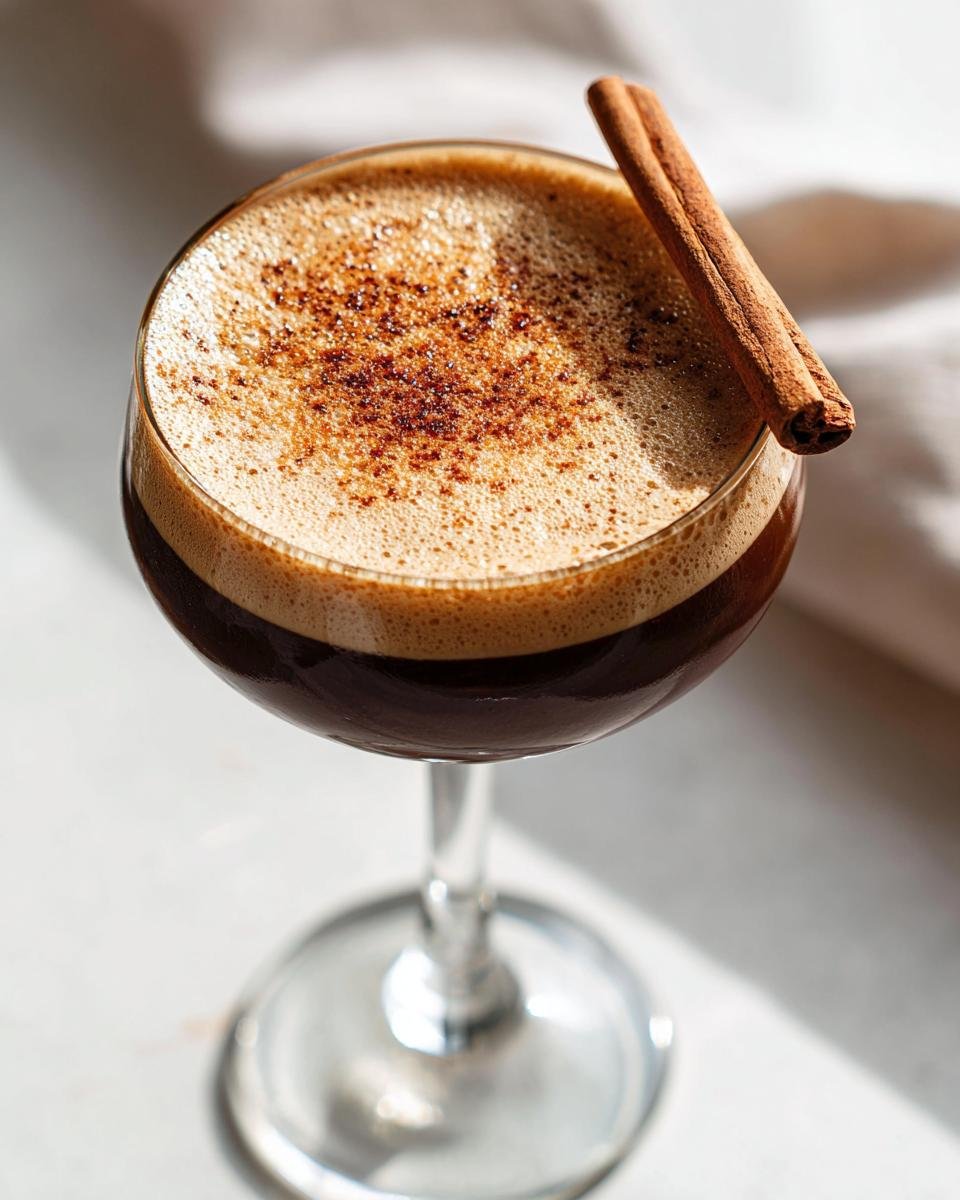 Close-up of a Maple Cinnamon Espresso Martini Mocktail with rich foam and a cinnamon stick garnish.