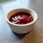 Close-up of My Favorite Gochujang Sauce, a thick, deep red sauce, served in a small white ramekin.