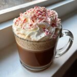 A clear mug filled with Peppermint White Chocolate Mocha, topped with whipped cream and crushed candy canes.