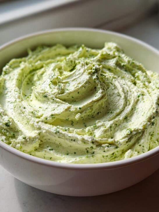 A white bowl filled with vibrant green Pesto Whipped Feta Dip, showing swirls on the surface.