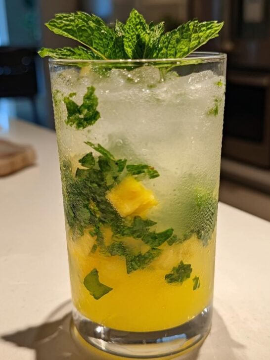 A tall, sweating glass filled with ice, pineapple chunks, and mint leaves for Pineapple Mint Lemonade.