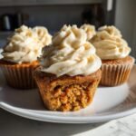 A close-up shot showing a bite taken out of one of the Pumpkin Chai Spiced Cupcakes, revealing the moist interior and creamy frosting.