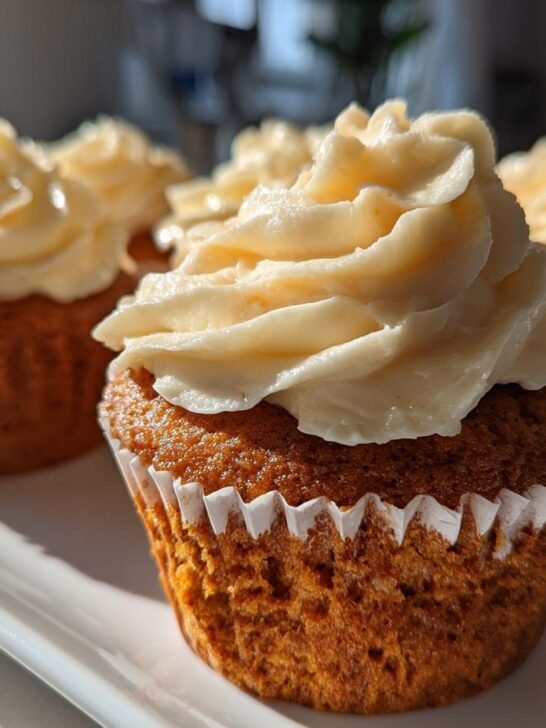 Close-up of freshly baked Pumpkin Chai Spiced Cupcakes topped with thick swirls of cream cheese frosting.