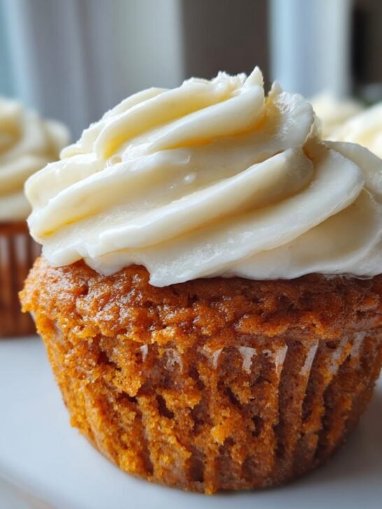 A close-up of one perfectly baked Pumpkin Cheesecake Cupcakes topped with thick, creamy white frosting.