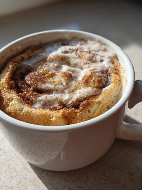 A close-up of a freshly made Pumpkin Cinnamon Roll Mug Cake topped with sweet icing.