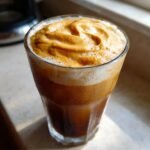 A tall glass of iced coffee topped with thick, rich orange Pumpkin Cold Foam Iced Coffee.