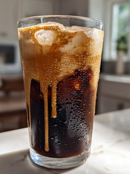 A tall glass of Pumpkin Cream Cold Brew Latte showing the rich dark coffee and dripping pumpkin cream topping over ice.