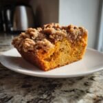 A close-up of a moist slice of Pumpkin Pecan Coffee Cake featuring a thick, crumbly streusel topping.