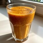 A close-up of a thick, orange Pumpkin Spice Smoothie in a textured glass, glistening with condensation.