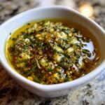 A close-up of the flavorful Roasted Garlic Olive Oil Dip, featuring minced garlic, herbs, and chili flakes suspended in golden olive oil.